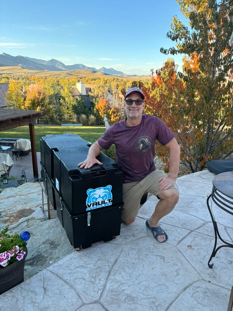 John Bye kneeling beside his Vault Sports Box cases on a patio, with the Colorado foothills behind