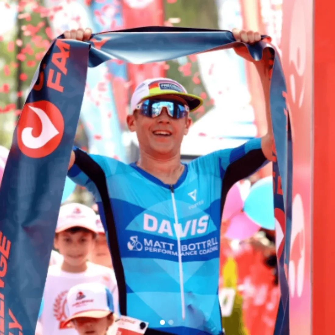Thomas Davis smiling as he holds the finish tape above his head at a Challenge race